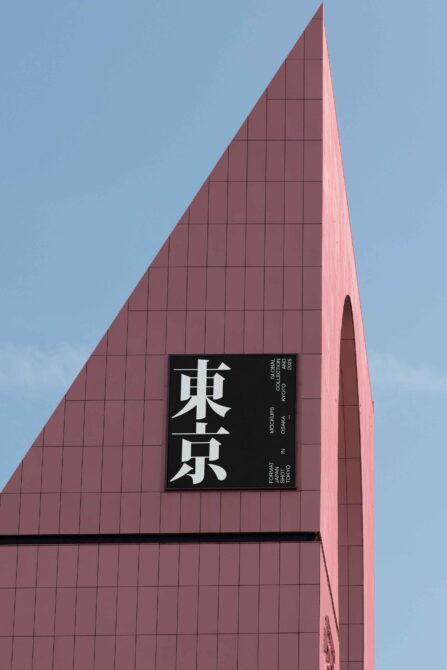 Black sign with white Japanese kanji mounted on pink triangular building facade