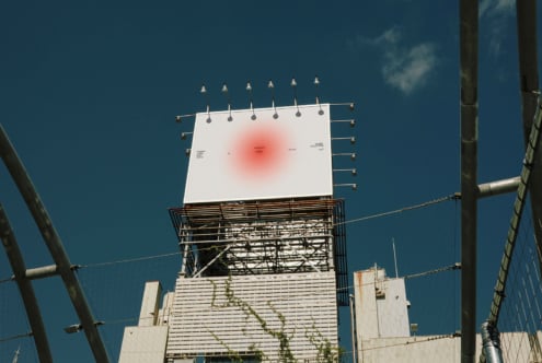Rooftop billboard lit by spotlights with soft red glow center on clear day