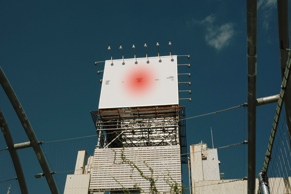 Rooftop billboard lit by spotlights with soft red glow center on clear day