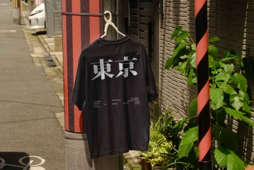 Black tee with white kanji characters on street backdrop with plants