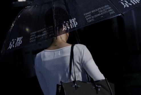 Person from behind holding dark umbrella with Japanese characters printed on canopy
