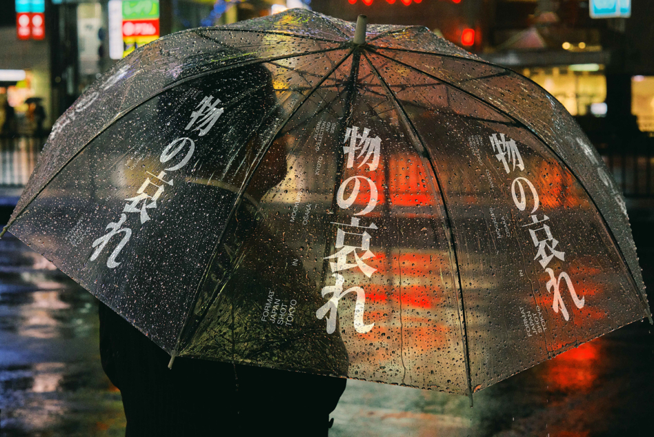 Clear umbrella with Japanese characters displayed against warm orange neon signs in urban setting