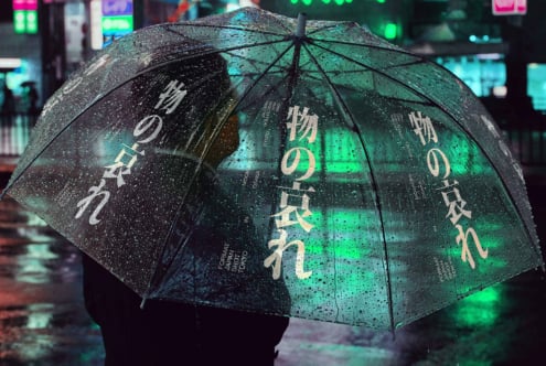 Clear umbrella with white kanji characters glowing under green neon street lighting at night