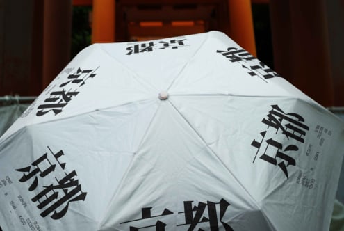 White umbrella with black Asian characters printed across panels, opened in front of orange architecture
