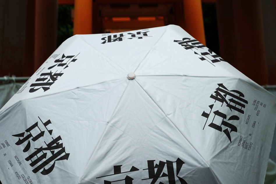 White umbrella with black Asian characters printed across panels, opened in front of orange architecture