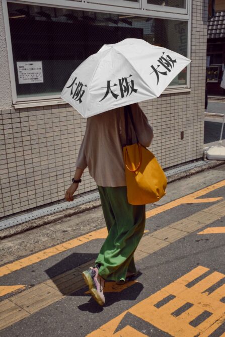 Woman with white umbrella Japanese characters yellow tote bag walking