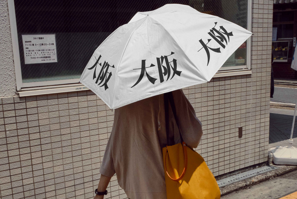 White umbrella with black kanji text carried by person in brown coat outdoors