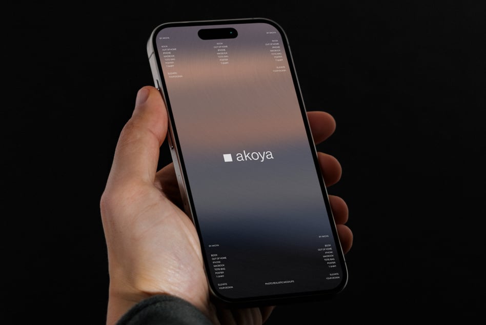 Hand holding iPhone against dark background displaying Akoya site with soft gradient design