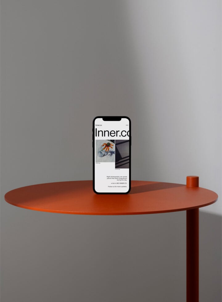 iPhone standing on rust-colored circular table with minimalist portfolio website displayed
