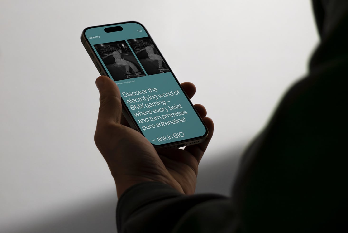 Hand holding iPhone displaying Inner.co teal website with BMX skateboarding imagery