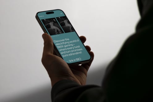 Hand holding iPhone displaying Inner.co teal website with BMX skateboarding imagery