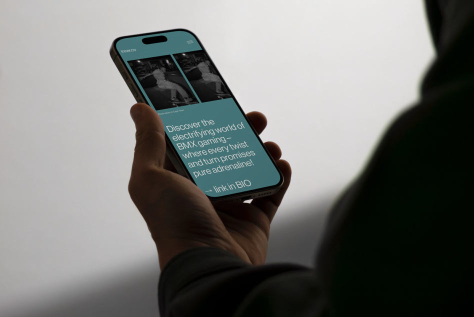 Hand holding iPhone displaying Inner.co teal website with BMX skateboarding imagery