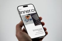 Hand holding iPhone displaying Inner.co website with portfolio grid layout on neutral background
