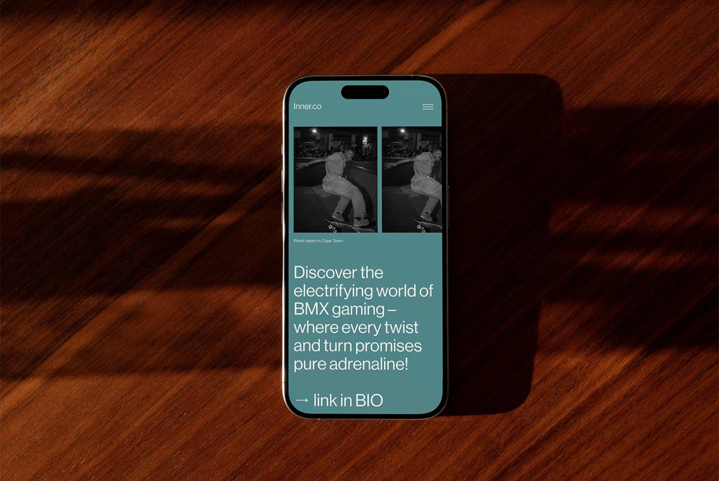 iPhone on wooden surface showing Inner.co teal interface with BMX gaming content