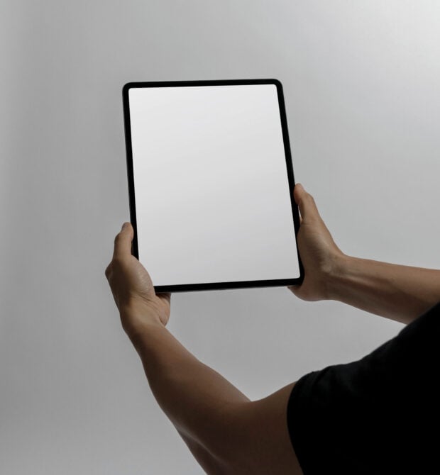 Hands holding tablet with blank white screen on neutral background