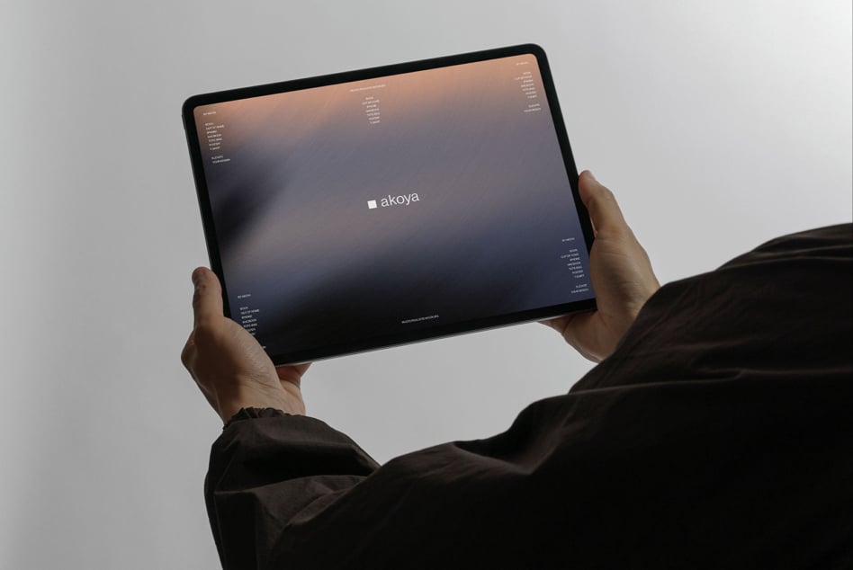 Hands holding tablet with dark gradient screen displaying akoya logo