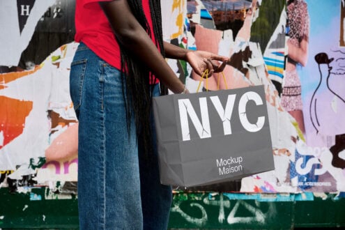 Hand holding gray tote bag with NYC logo in front of colorful street mural
