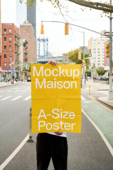 Yellow A-size poster mockup held on busy city street with Manhattan Bridge behind