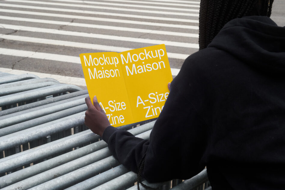 Person holding yellow zine mockup on concrete steps with striped railing