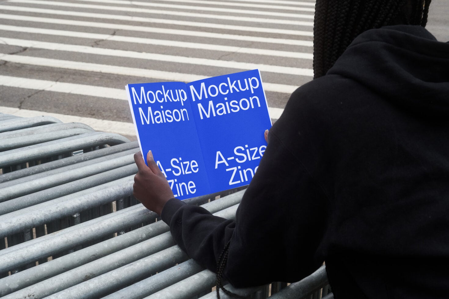 Person holding blue zine mockup on concrete steps with striped railing
