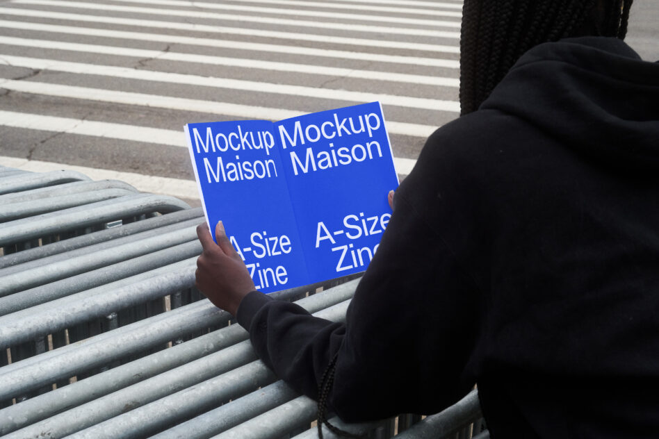 Person holding blue zine mockup on concrete steps with striped railing