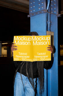 Person holding yellow tabloid newspaper mockup in front of metal structure