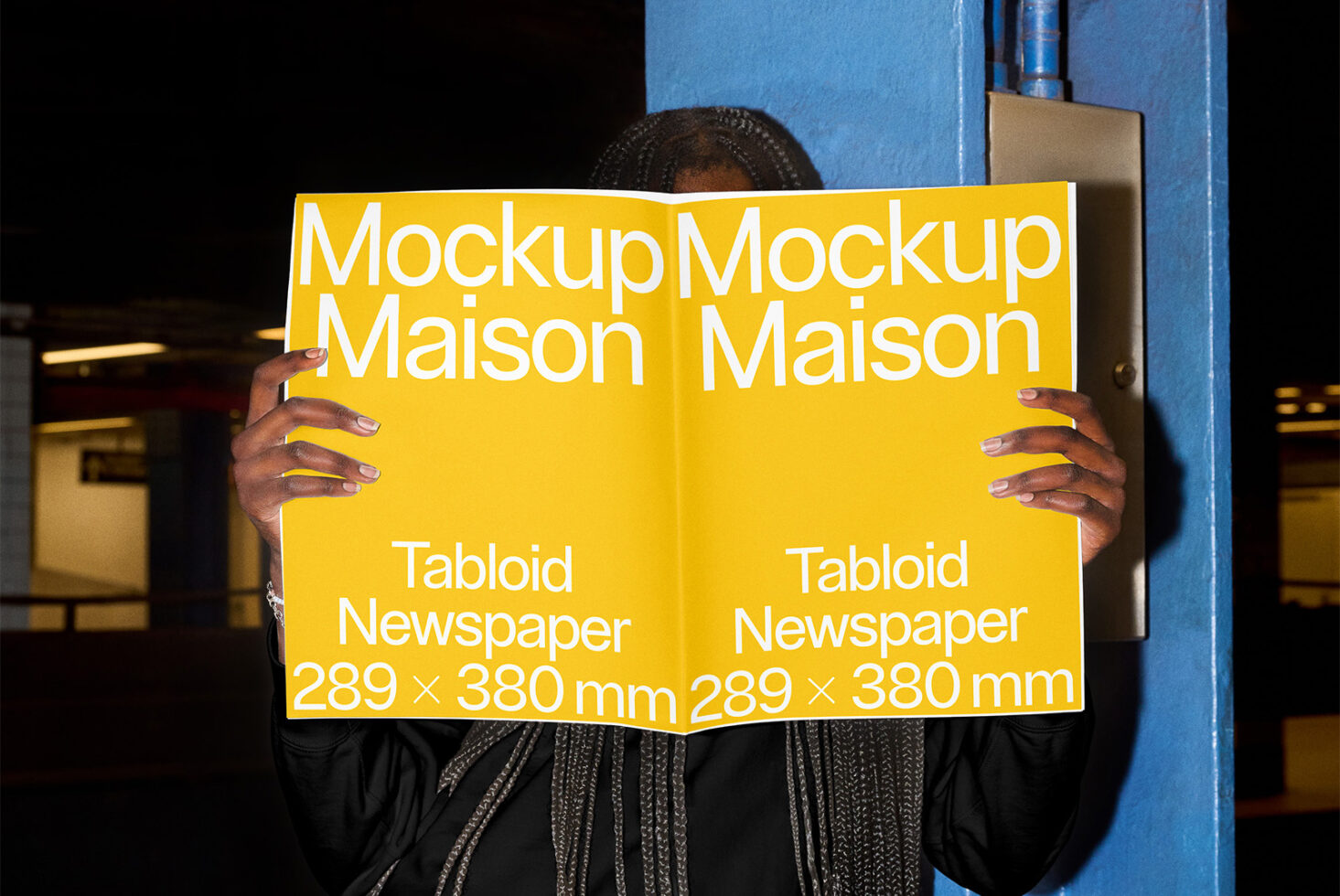 Person holding open yellow tabloid newspaper mockup in industrial setting