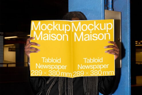 Person holding open yellow tabloid newspaper mockup in industrial setting