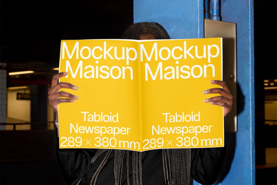 Person holding open yellow tabloid newspaper mockup in industrial setting