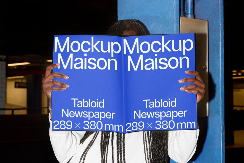 Person holding blue tabloid newspaper mockup in front of blue metal structure