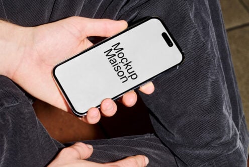 Hand holding iPhone with light screen mockup against dark jacket