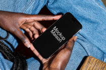 Hands holding iPhone with black screen in front of light blue denim pants