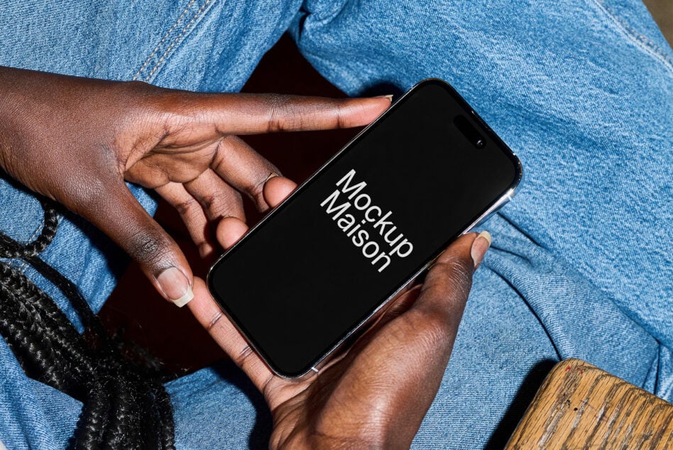 Hands holding iPhone with black screen in front of light blue denim pants