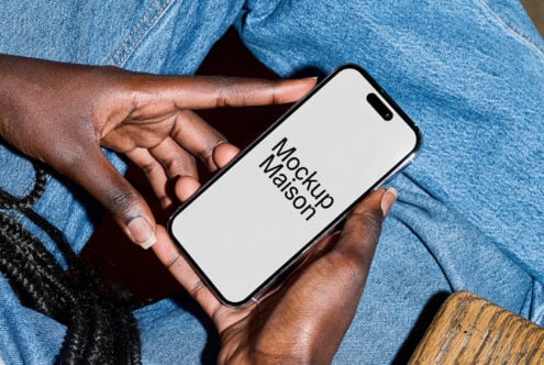 Hands holding iPhone with white screen in front of light blue denim pants