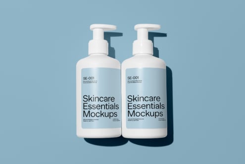 Skincare essentials packaging mockup featuring two white pump bottles with blue labels on a blue background ideal for cosmetic branding and design projects.