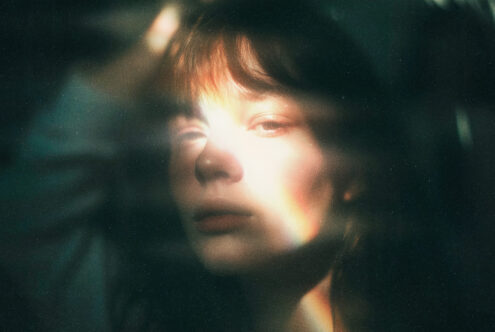 Dreamy soft focus portrait with bright light flare against dark teal background