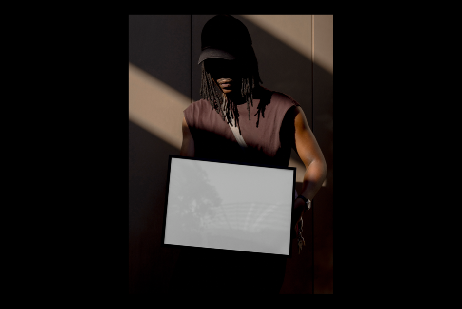 Person holding blank poster frame in shadowed setting suitable for mockups and design previews. Keywords: mockup template, poster design, graphics.