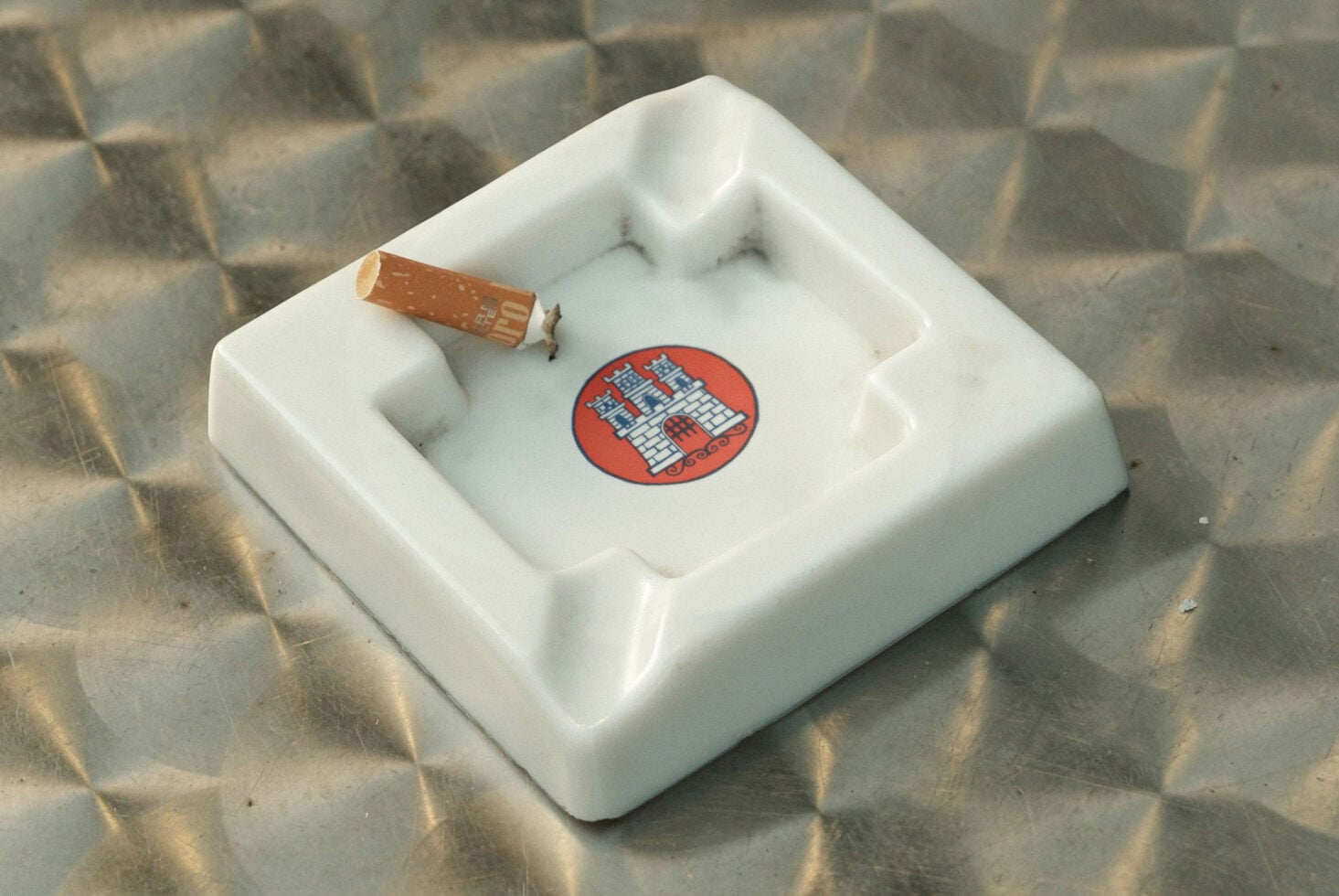 White ceramic ashtray mockup with red circular logo badge, cigarette resting on rim