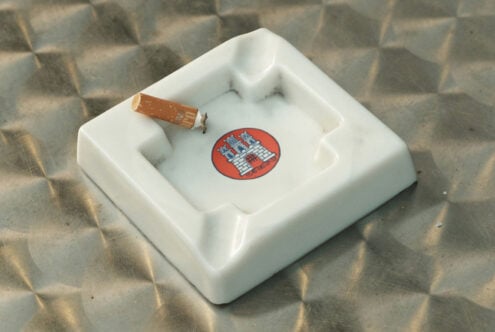 White ceramic ashtray mockup with red circular logo badge, cigarette resting on rim
