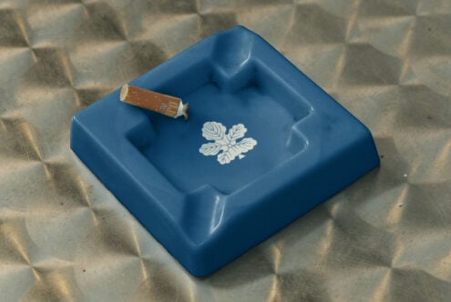 Blue ceramic ashtray with cigarette, white leaf motif printed in center square