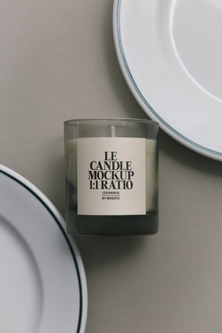 Glass candle with cream label, ceramic plates in soft focus