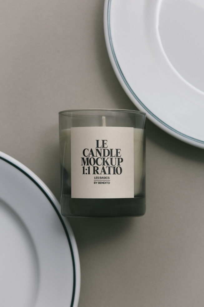 Glass candle with cream label, ceramic plates in soft focus