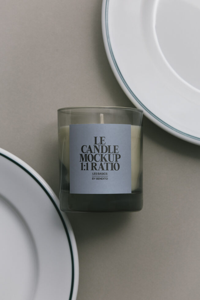 Glass candle with light blue label, ceramic plates in soft focus