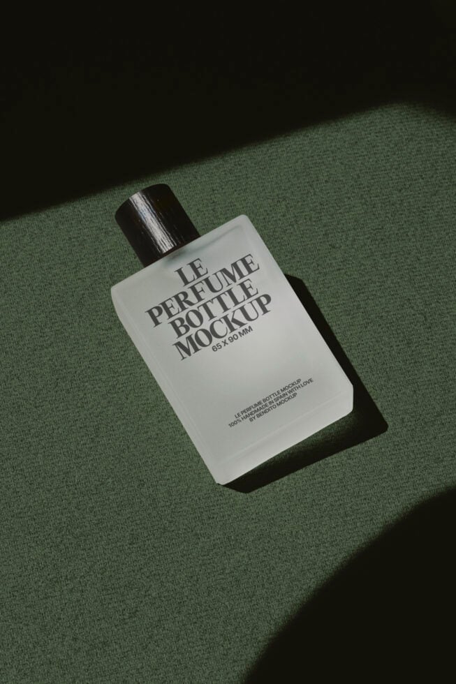 Minimalist white perfume bottle with black cap on sage green fabric background, sunlit