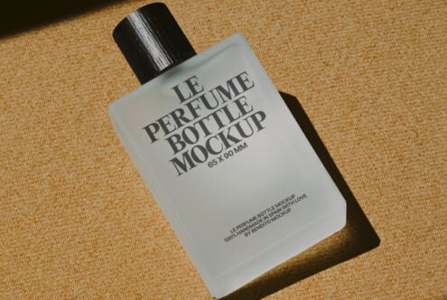 White cologne bottle with black spray cap on warm sand colored woven textile background