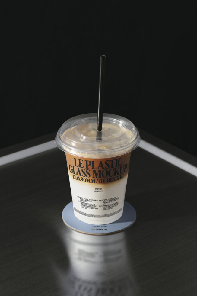 Clear plastic takeout cup with straw filled with tan beverage on dark surface