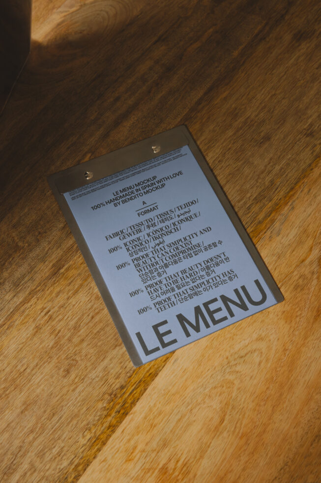 Menu mockup on wood surface with metal clips at top, multilingual text layout