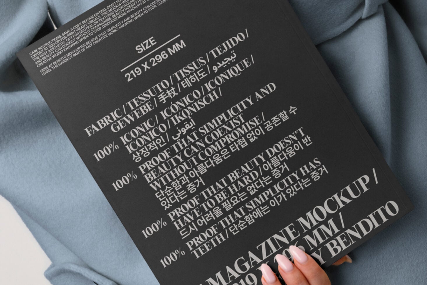 Dark magazine mockup with multilingual text held against blue-gray oversized blazer