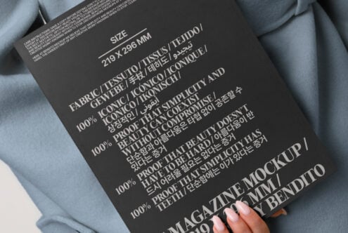 Dark magazine mockup with multilingual text held against blue-gray oversized blazer