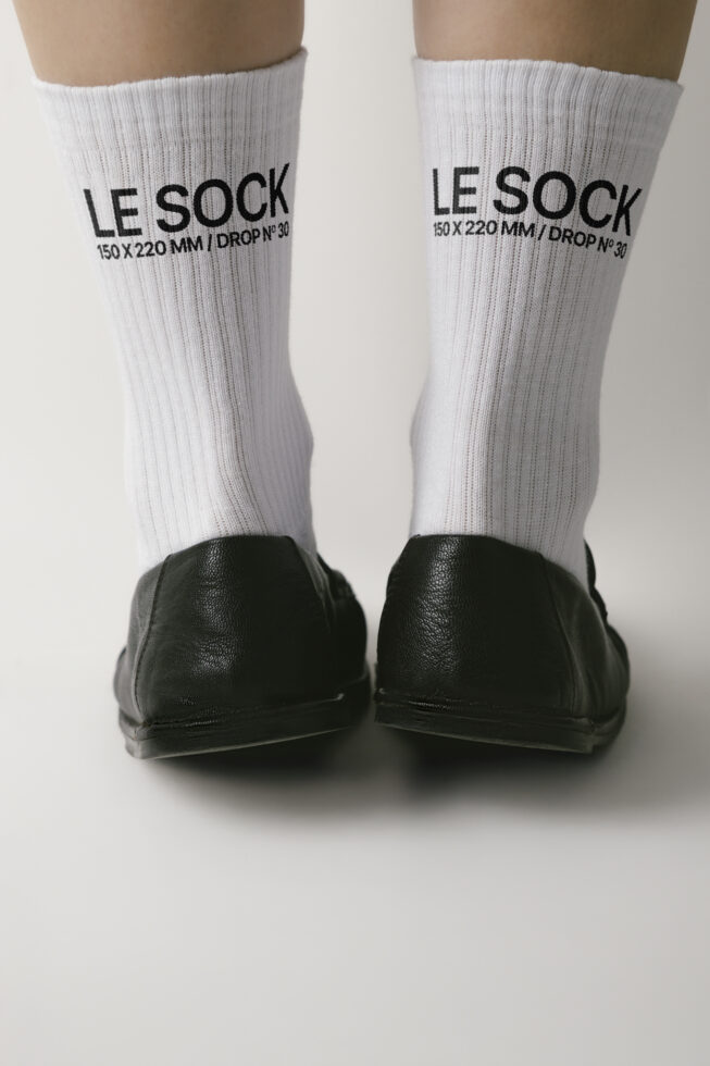 White ribbed crew socks on feet with black embroidered branding